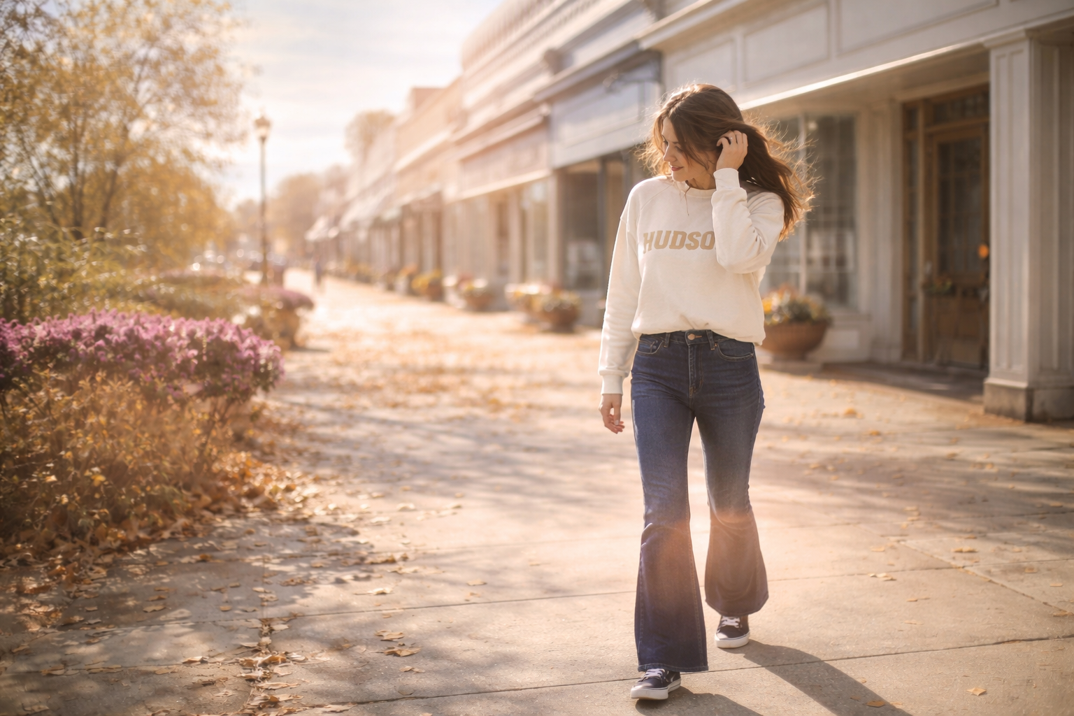 Woman walking down downtown Hudson Ohio street in fall wearing neutral sweatshirt and denim with sunlight and wind movement